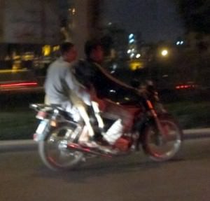 Two men and a goat on a bike in midnight traffic